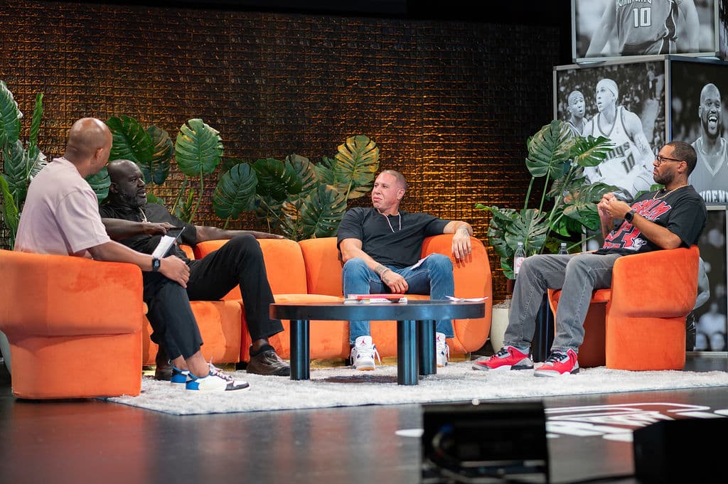 Shaquille O’Neal and guests seated on an orange set during a live podcast taping